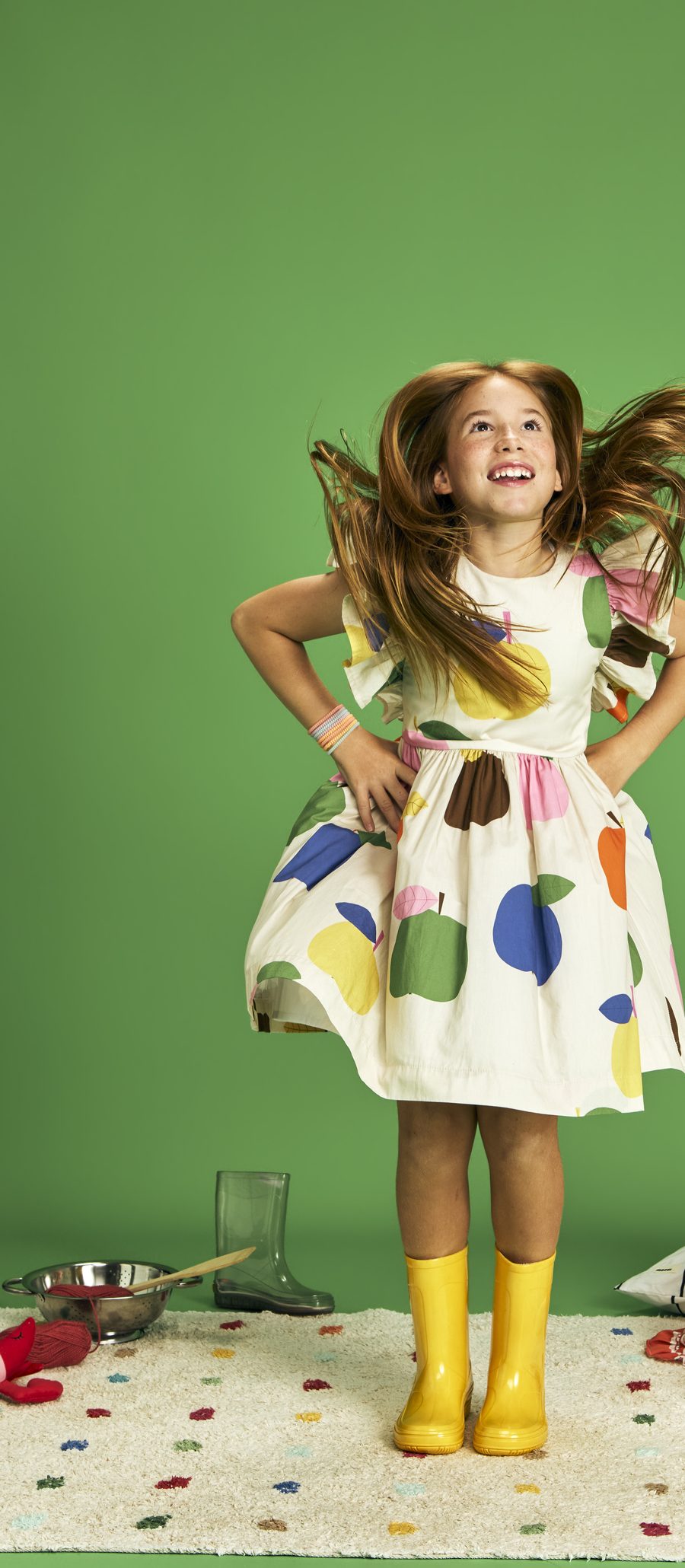 Menina de botas amarelas sorrindo com o cabelo em movimento, sobre fundo verde